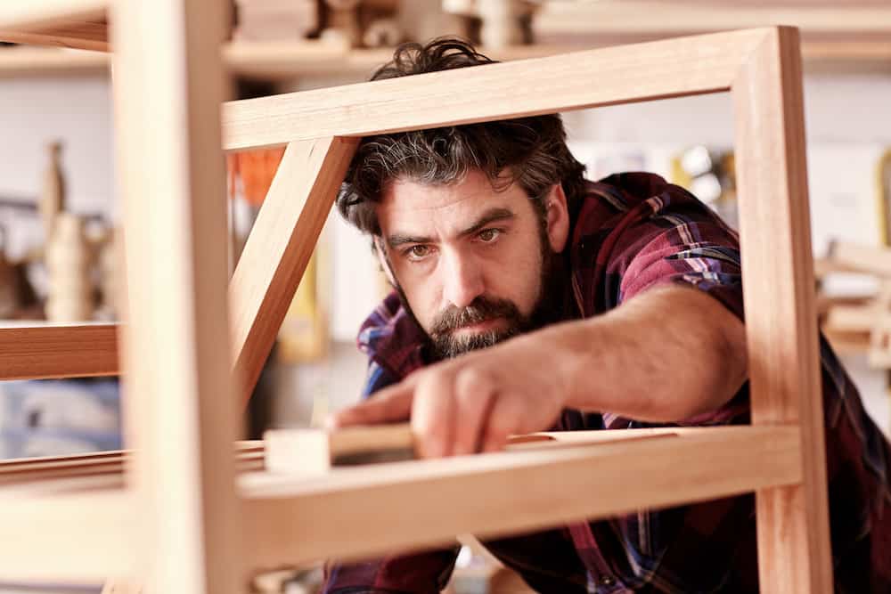 Craftsman sanding a wooden item in his woodwork studio what is the best wood for outdoor furniture