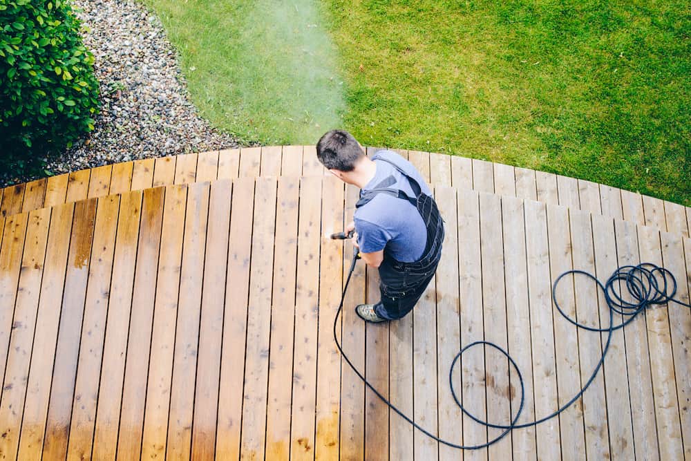 man cleaning terrace with a power washer - high water pressure cleaner on wooden terrace tips on how to winterize a pressure washer