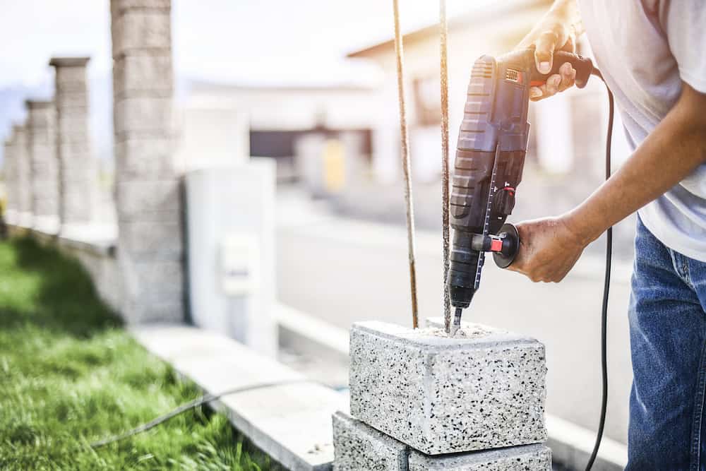 Man worker with pneumatic hammer or drill perforator equipment making hole in bricks wall at construction. do i need a hammer drill facts